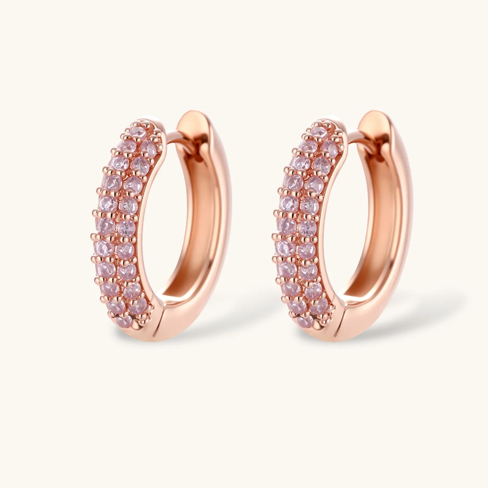 Rose gold pavé zirconia bar necklace, hoop earrings, and open ring set with pink stones on cream background.