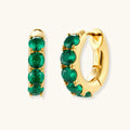 Close-up of gold-plated huggie hoop earrings featuring four emerald green cubic zirconia stones on white background.