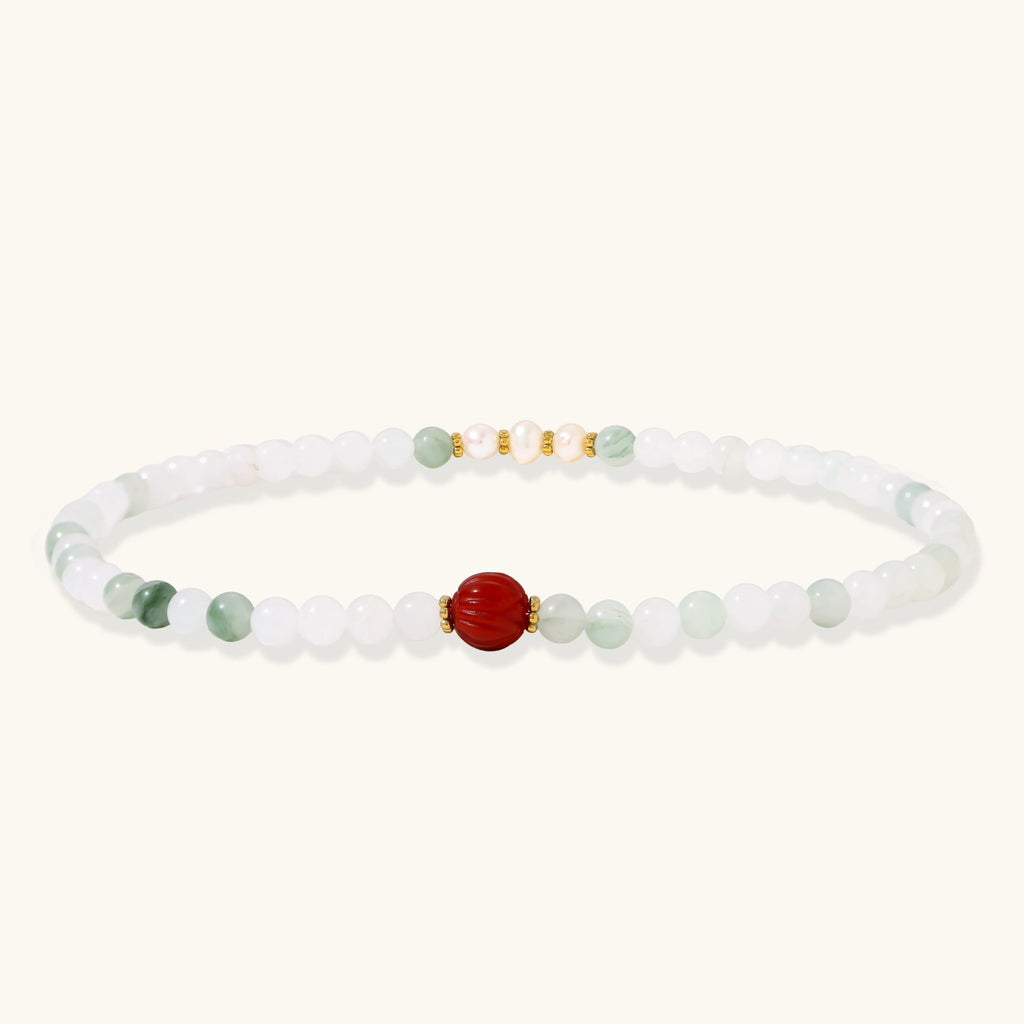 Three layered white beaded bracelets with carved orange agate lotus centerpiece and freshwater pearls on cream background.